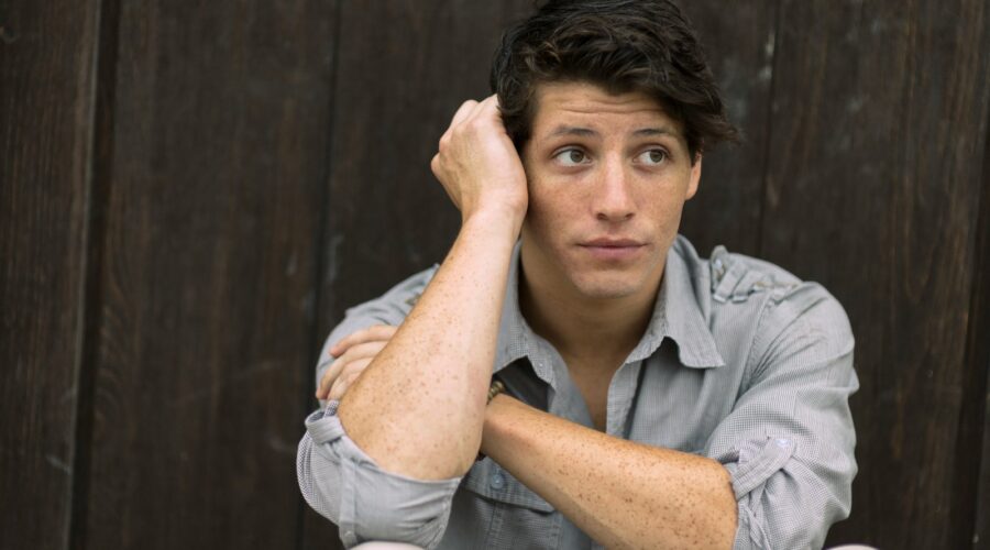 man wearing gray dress shirt leaning on brown wall