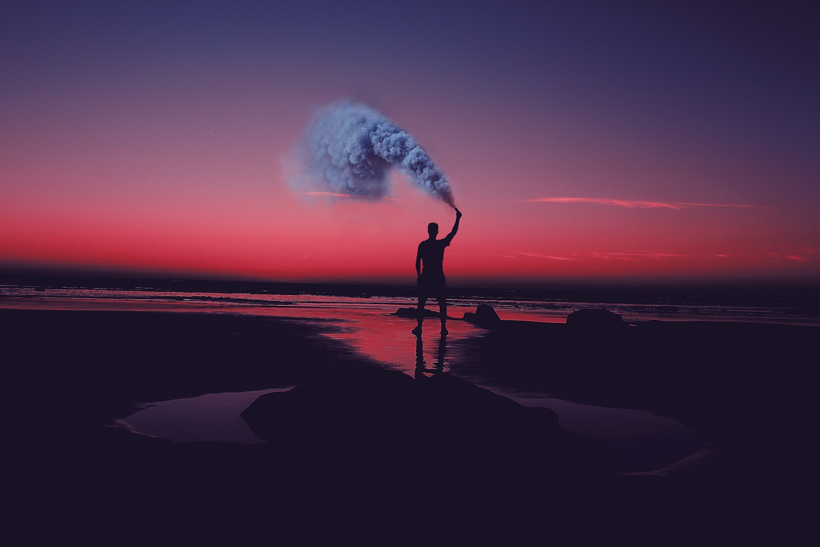 silhouette of man standing on seashore holding smoke can