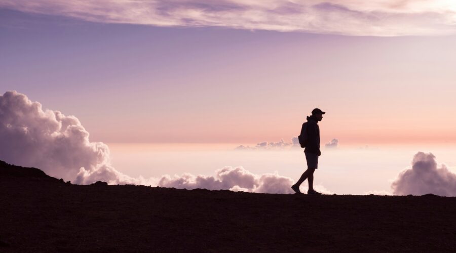 silhouette of person walking under white clouds