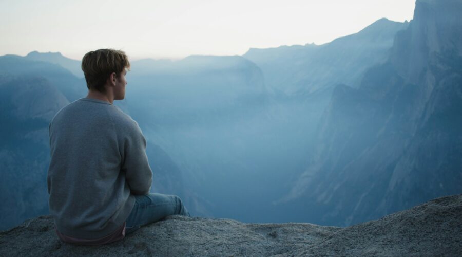 man in gray shirt sits on cliff