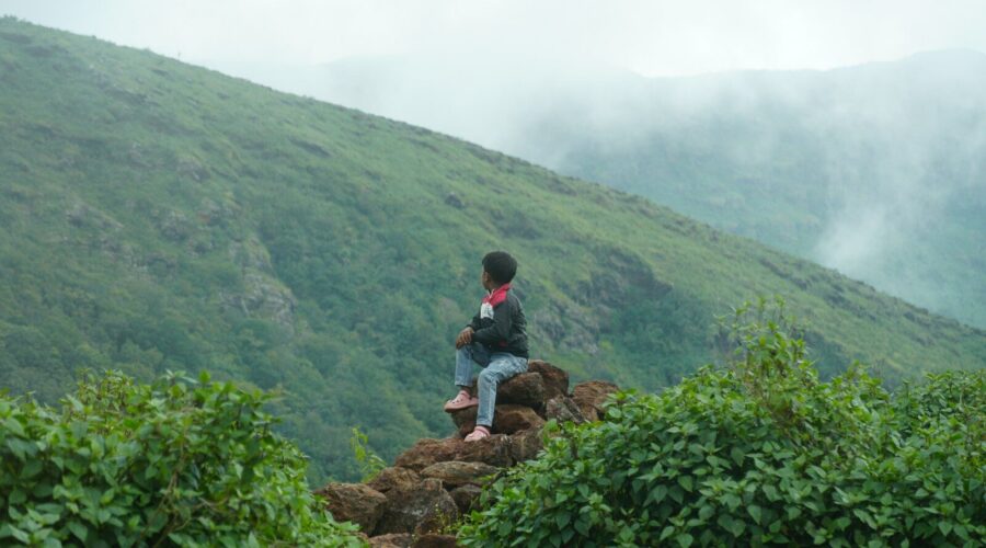 Person sitting on rocks overlooking misty mountains