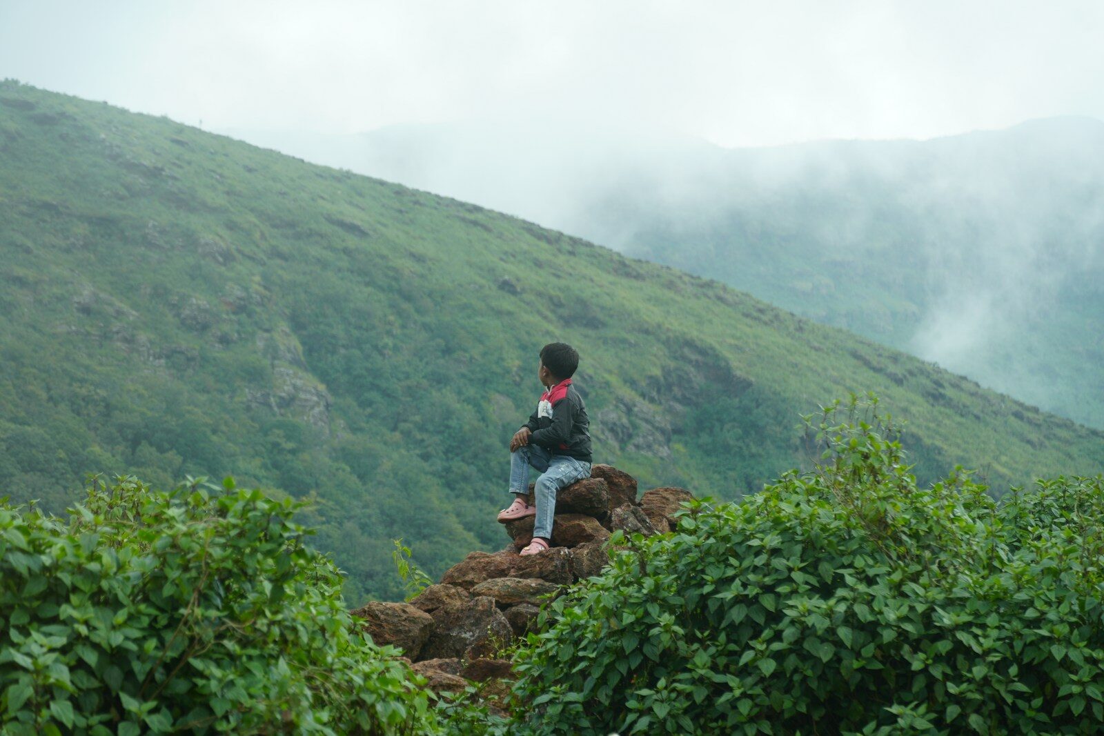 Person sitting on rocks overlooking misty mountains
