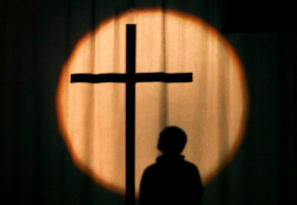 Photo by Jametlene Reskp a silhouette of a person standing in front of a cross